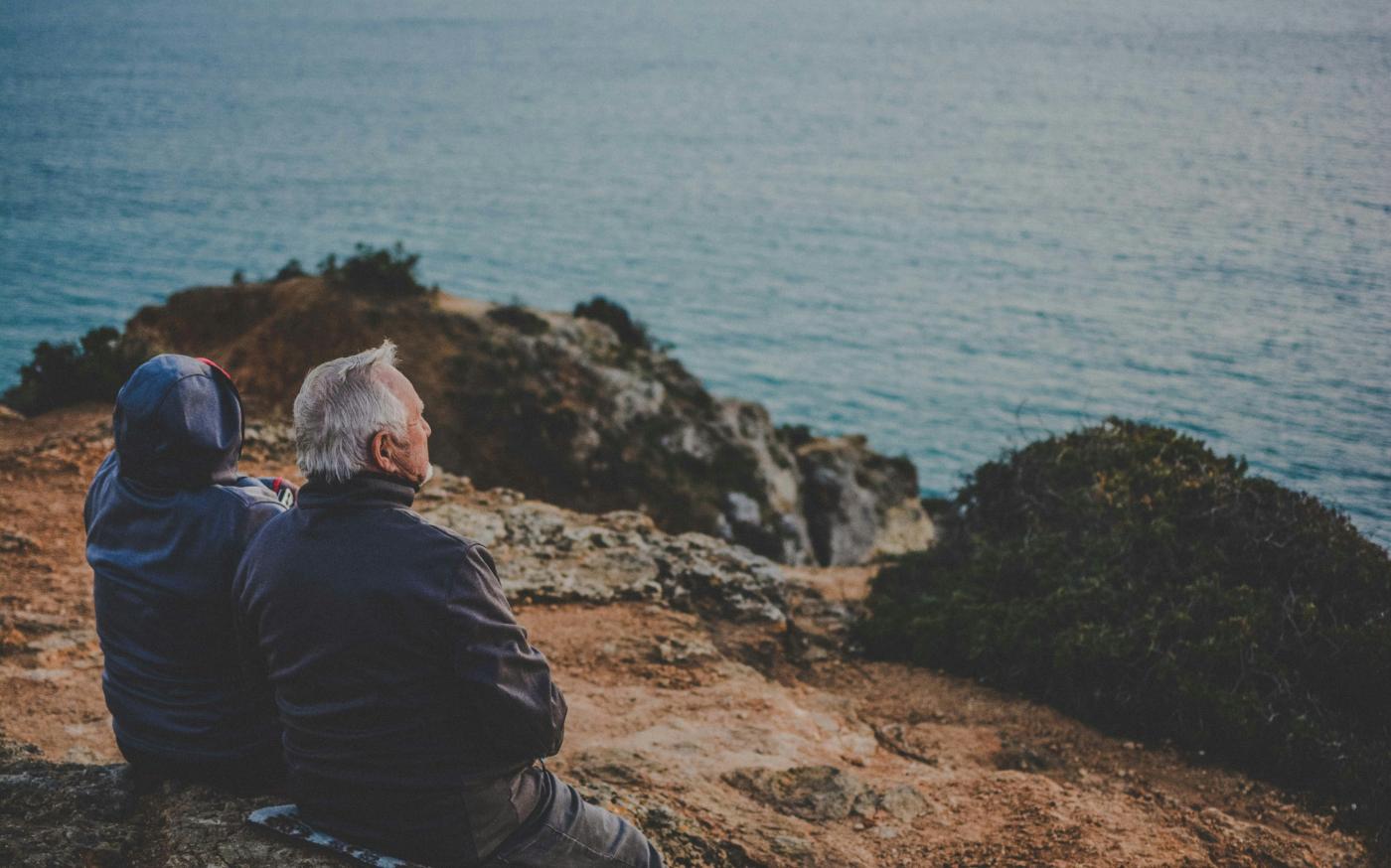 two person sitting on rock staring at body of water during daytime by Katarzyna Grabowska courtesy of Unsplash.